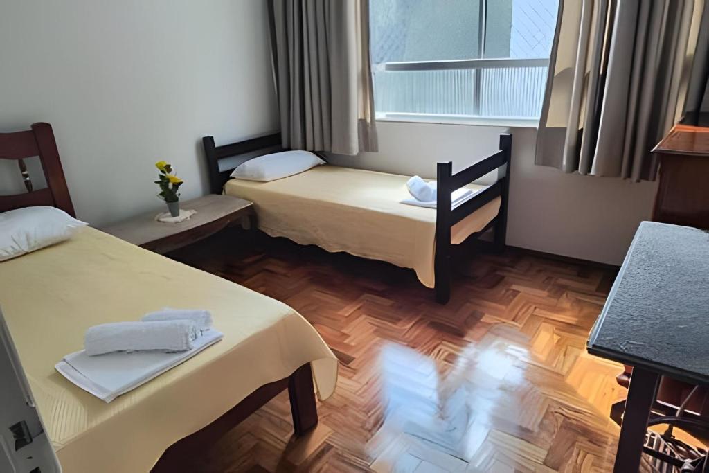 a small room with two beds and a window at Apto Clássico, Centro de Friburgo, em frente à Pça Getúlio Vargas e pertinho do Teleférico e da Pça Suspiro - Muito bem equipado - Aquecedor in Nova Friburgo