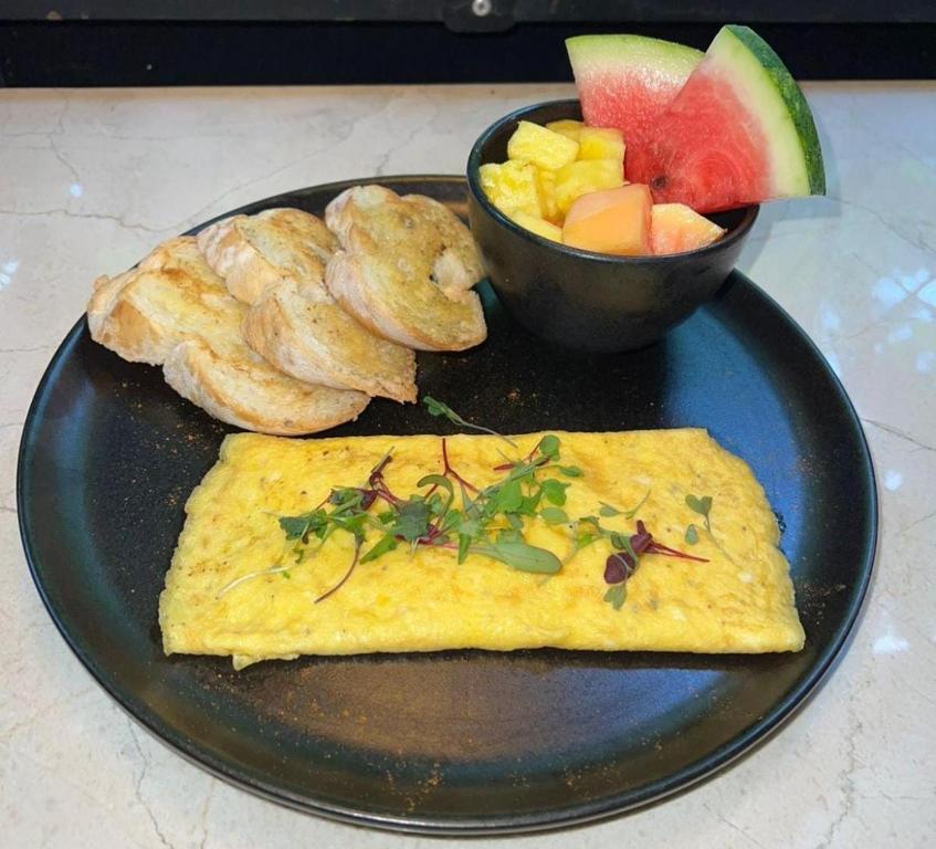 メデジンにあるHotel Living 35 Suites Piso 8 Vipのオムレツとフルーツのボウルが乗った黒い皿