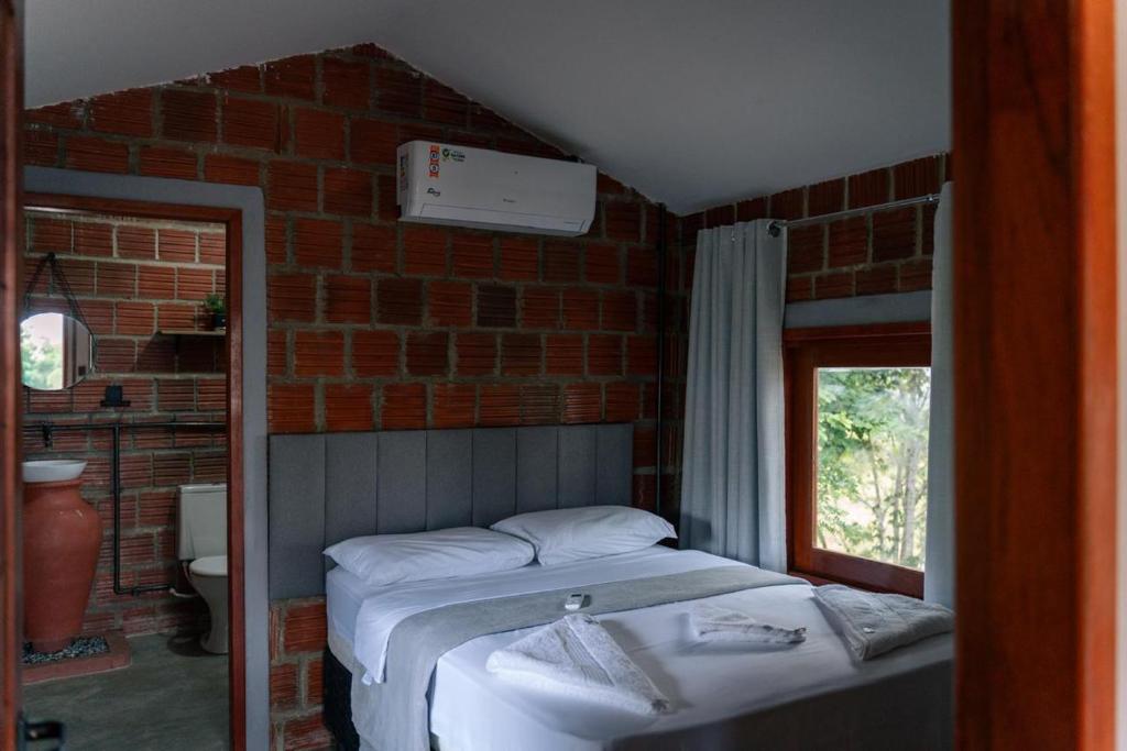 une chambre avec un lit et un mur de briques dans l'établissement Ecoville Coracao da Serra, à Areia