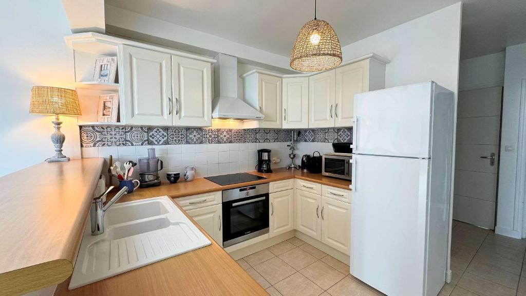 Una cocina con gabinetes blancos y un refrigerador blanco. en Charmante location à deux pas de la plage, en Rivedoux-Plage