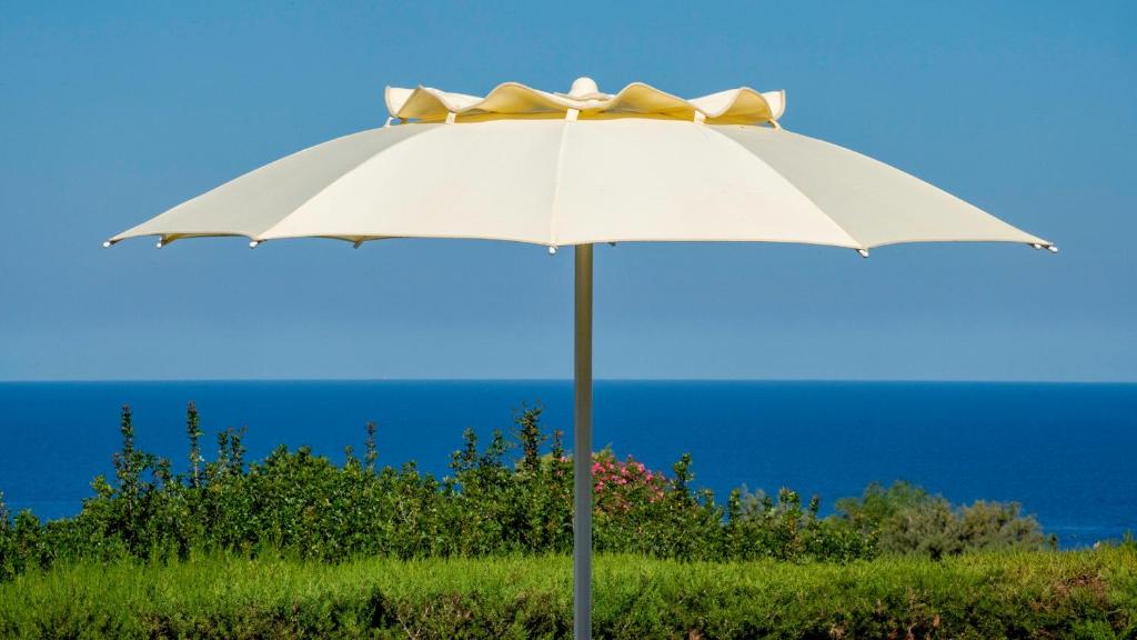 a white umbrella sitting in the grass near the ocean at Li Chessi Blu Villetta Familiare con Piscina in Costa Paradiso