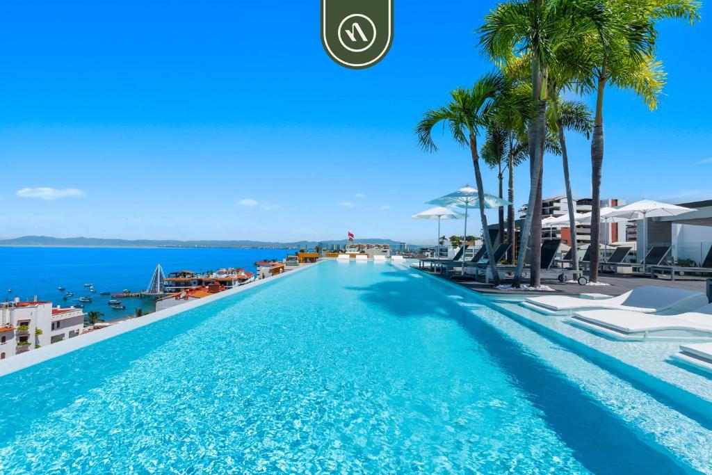 a swimming pool at the beach with palm trees and the ocean at Amazing 1 BR Condo in Romantic Zone - Pool - Gym in Puerto Vallarta