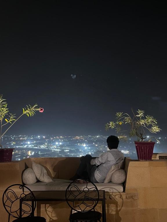 un homme assis sur un canapé regardant la ville la nuit dans l'établissement Hotel Surja Jaisalmer, à Jaisalmer