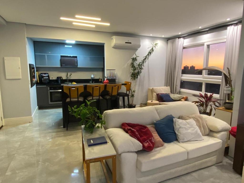 a living room with a white couch and a kitchen at Belíssimo apartamento em Porto Alegre! in Porto Alegre