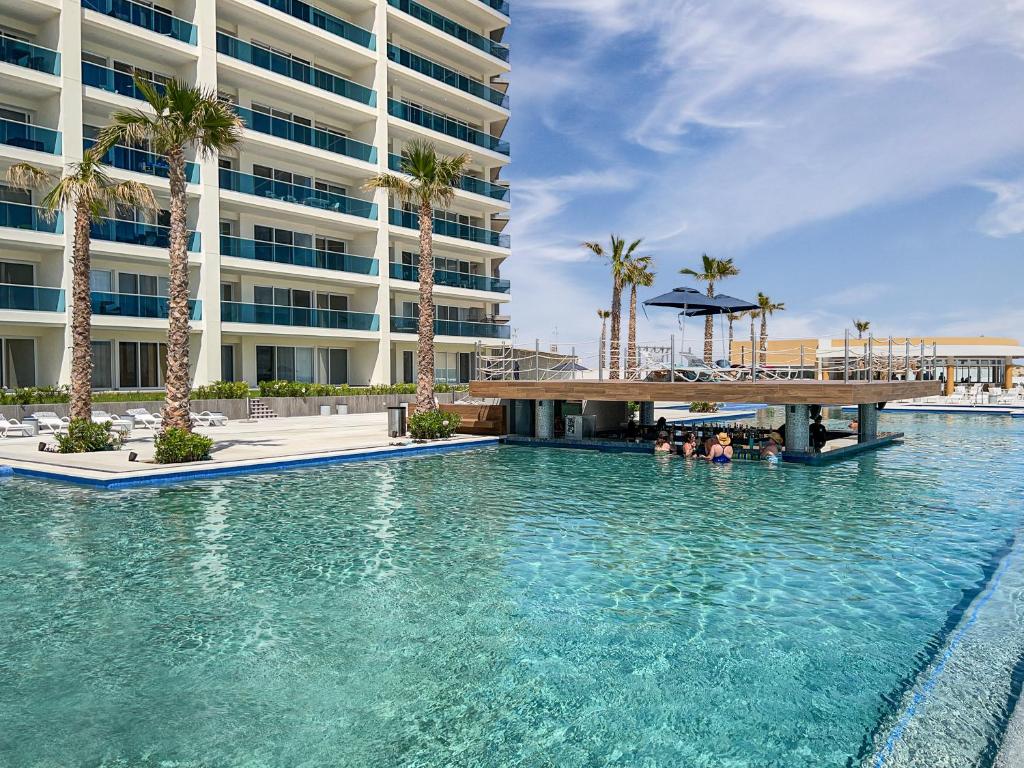 a swimming pool in front of a building with palm trees at Splash in The New Lazy River and Sleep In Luxury Encantame Towers Velero 2202 in Playa Encanto
