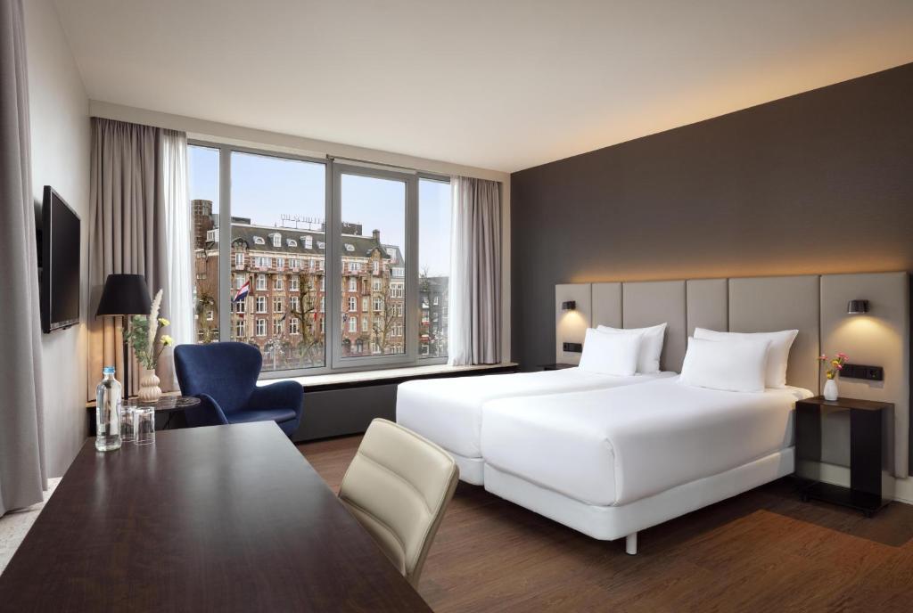 a hotel room with a white bed and a table at NH Amsterdam Caransa in Amsterdam
