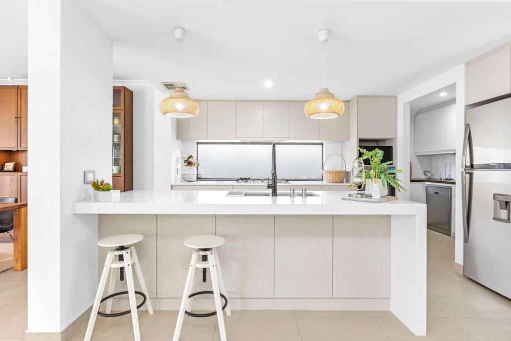 a kitchen with white cabinets and stools at Coastal Retreat in Burns Beach in Kinross