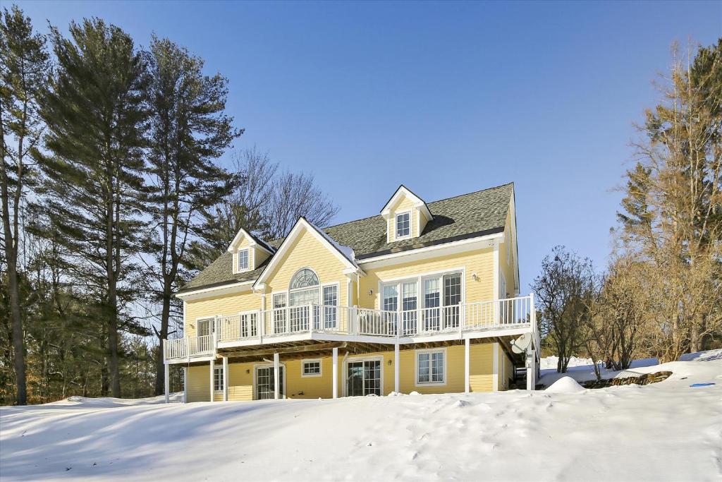 a yellow house with a balcony in the snow at Weeks Hill: 5 br, fireplace, a/c, deck, views! in Stowe