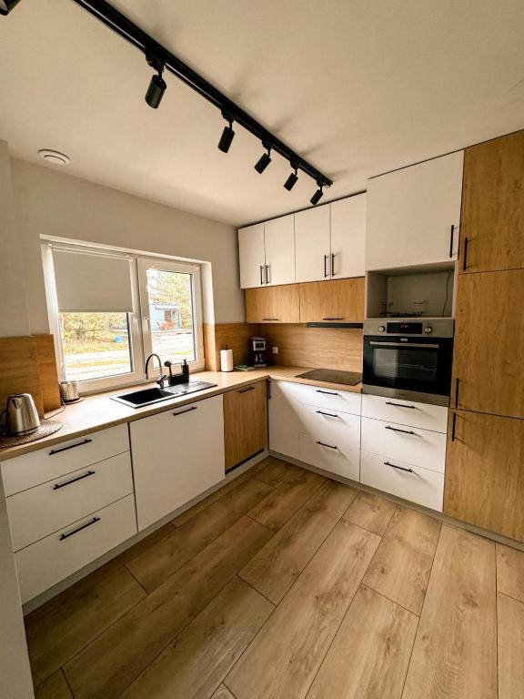 Il comprend une cuisine avec des placards blancs, du parquet et une fenêtre. dans l'établissement Apartamenty Brzozowe, à Okoniny Nadjezierne