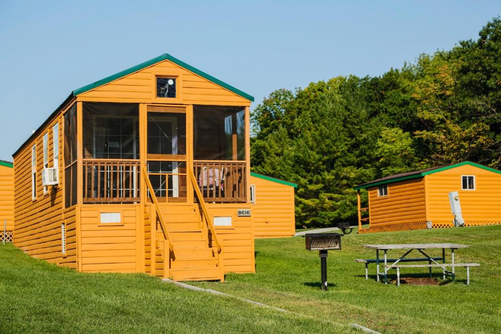 a large wooden cabin with a picnic table in the grass at Plymouth Rock Camping Resort Rustic Cabin in Elkhart Lake