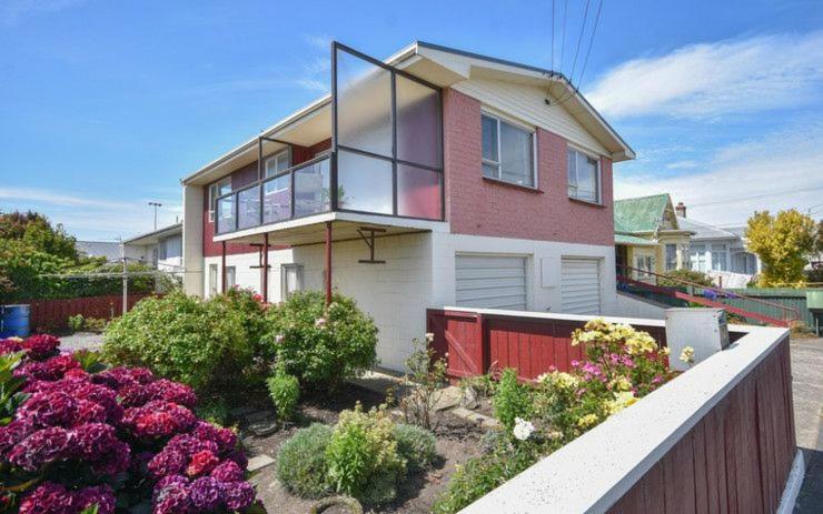 ein Haus mit einem Zaun und Blumen davor in der Unterkunft Beachside Townhouse Dunedin in Dunedin