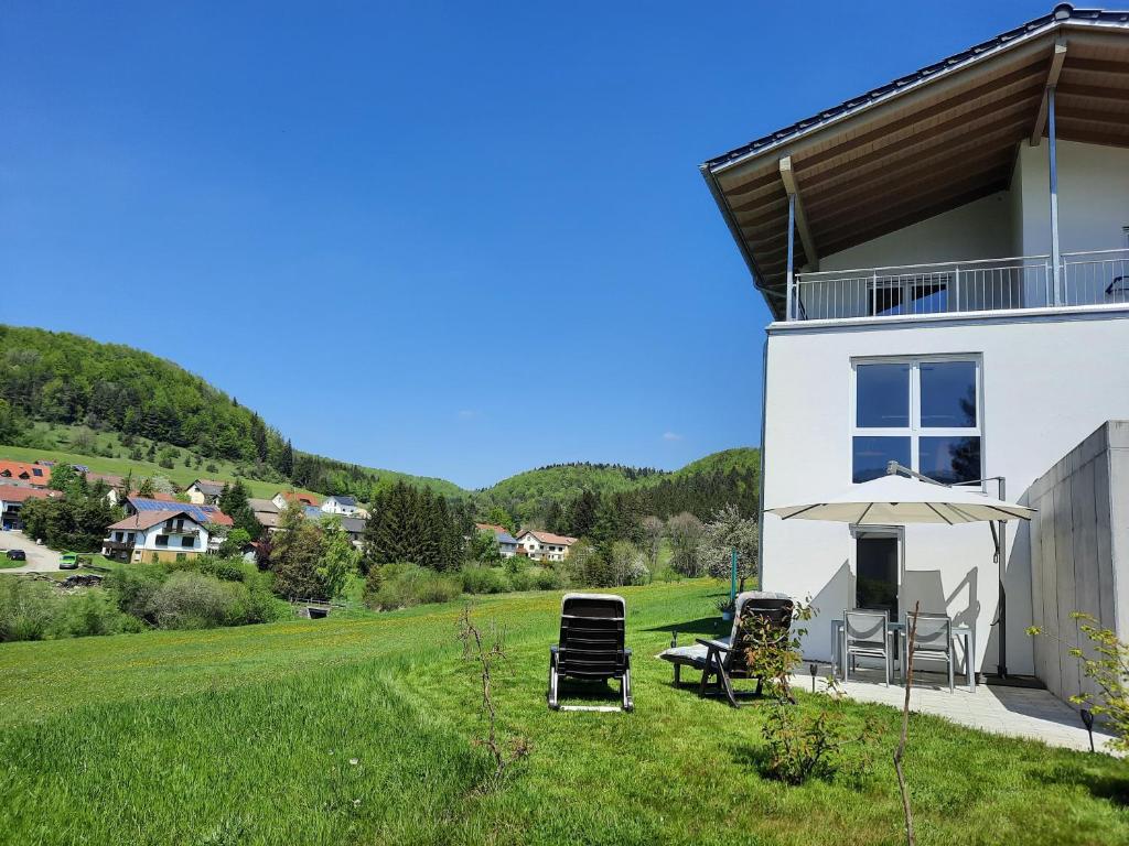 a white house with chairs and an umbrella at Ferienwohnung Im Eyachtal in Albstadt