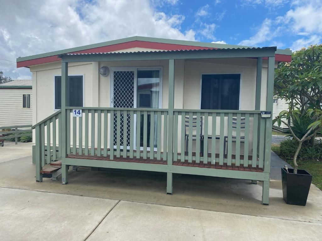 una pequeña casa verde y blanca con porche en Maclean Riverside Caravan Park, en Maclean