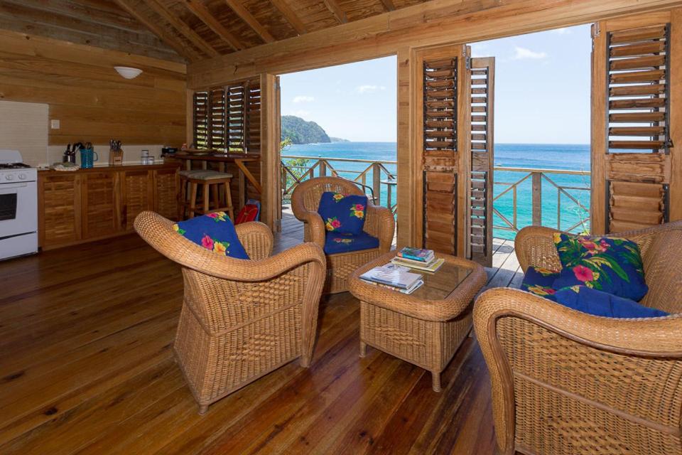 a living room with wicker chairs and a kitchen with the ocean at SeaScape on Heavenly Bay in Castara