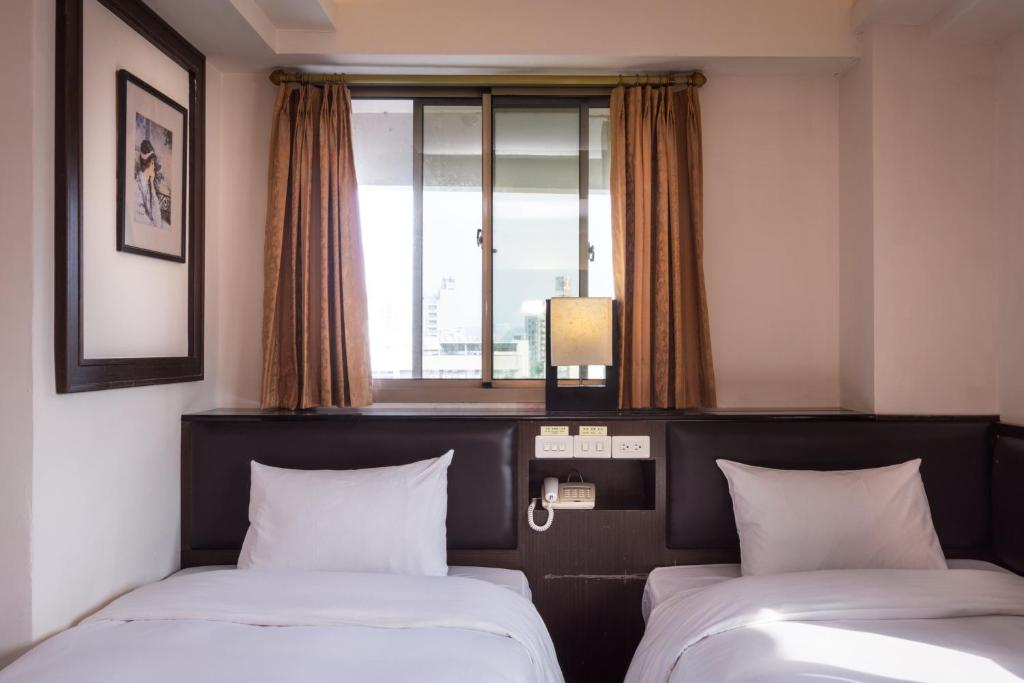 two beds in a hotel room with a window at The Enterpriser Hotel in Taichung