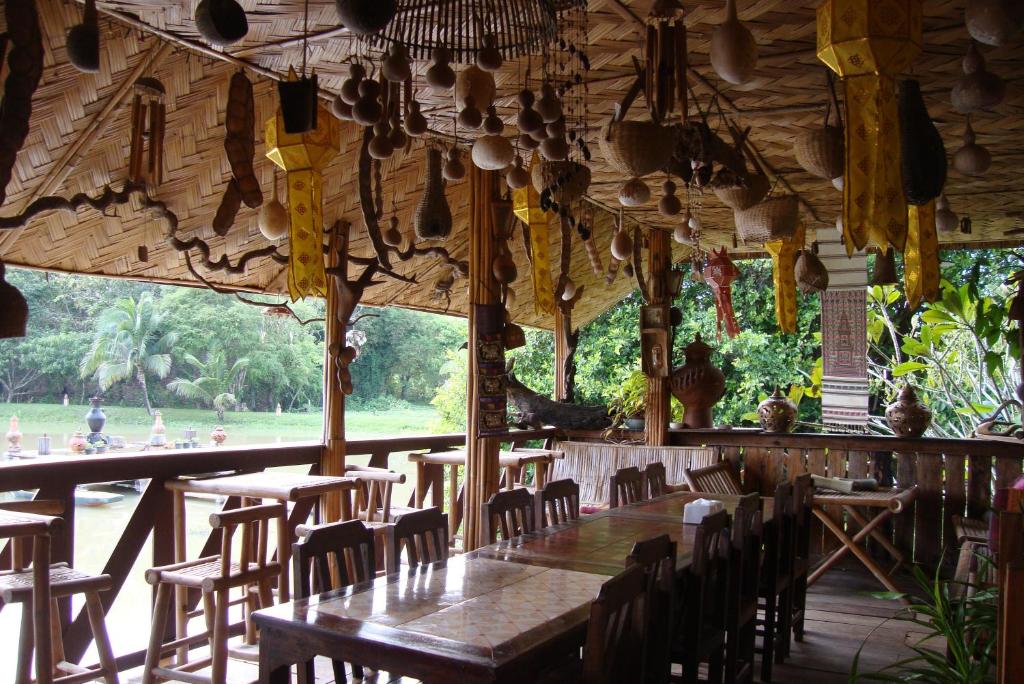 a restaurant with wooden tables and chairs and a large window at Baan Suan Jantra Home Stay in Chiang Rai