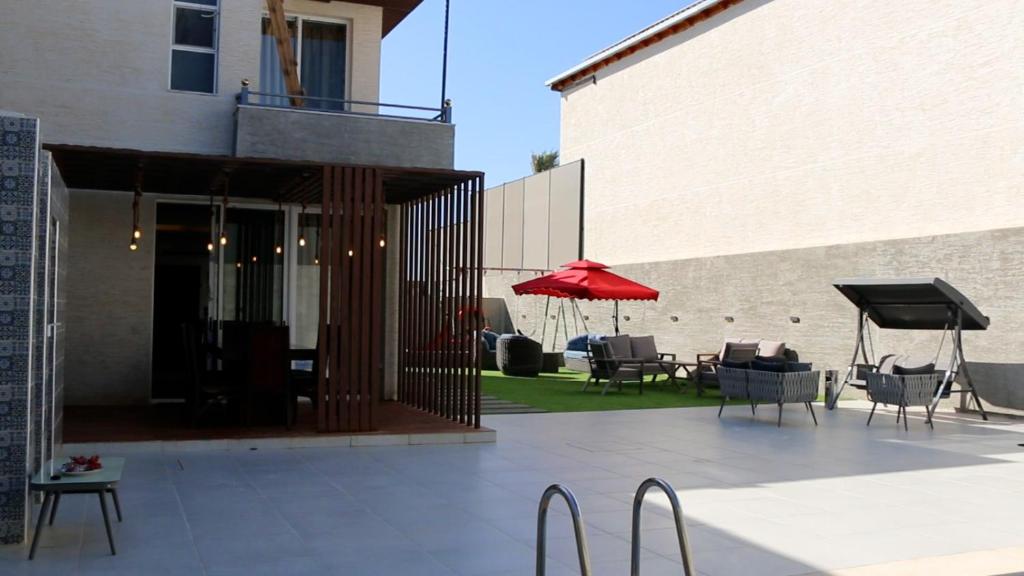 eine Terrasse mit Stühlen und einem roten Sonnenschirm neben einem Gebäude in der Unterkunft شاليه ولا بالأحلام in Al Rama