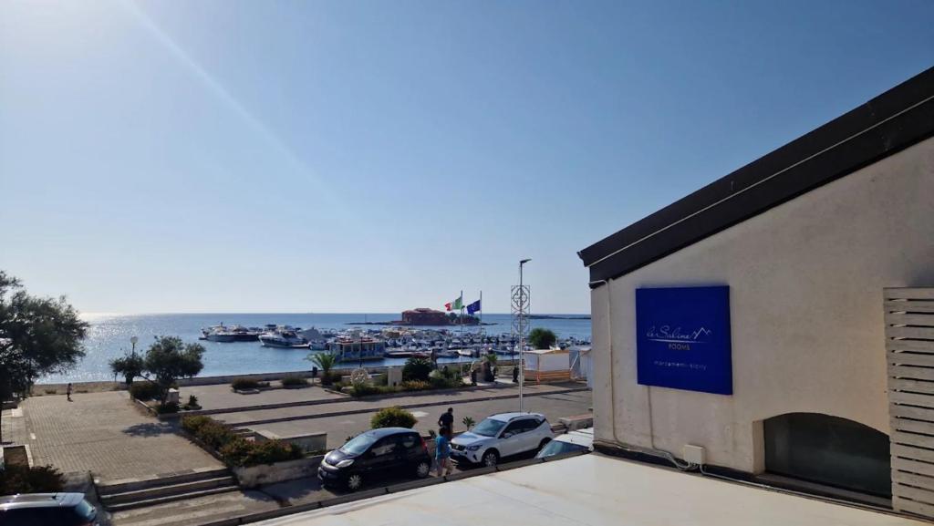 a building with cars parked in a parking lot next to the water at Le Saline Rooms Marzamemi in Marzamemi