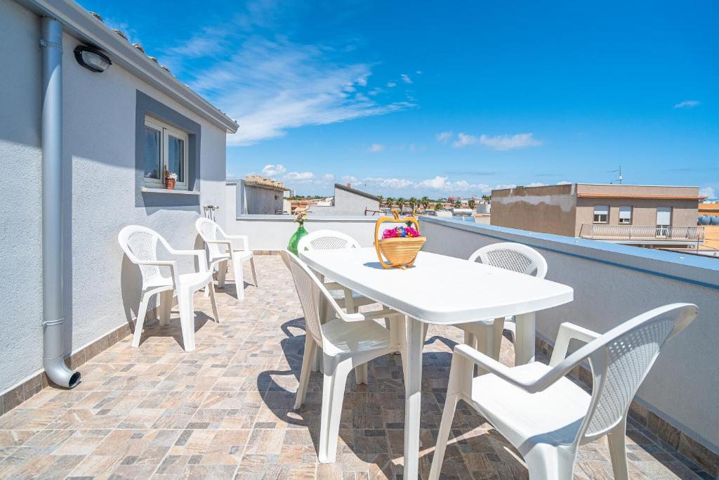 un patio con sillas blancas y una mesa en el balcón en Le Quattro Perle Apartments, en Pachino