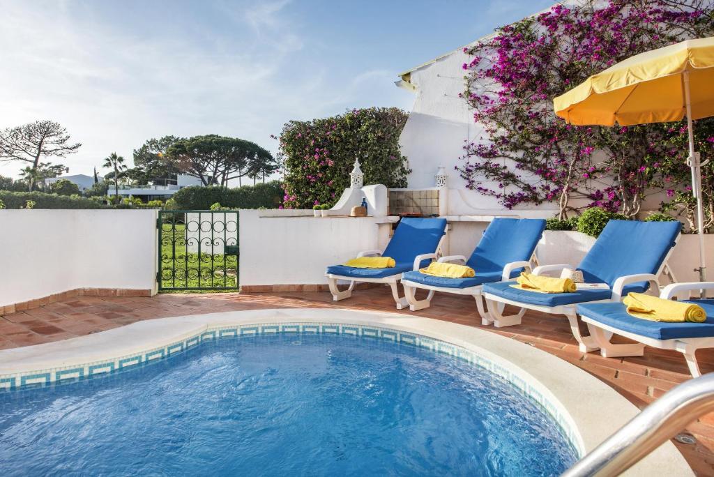 a swimming pool with blue chairs and an umbrella at Mng Elliott42 in Vale do Lobo