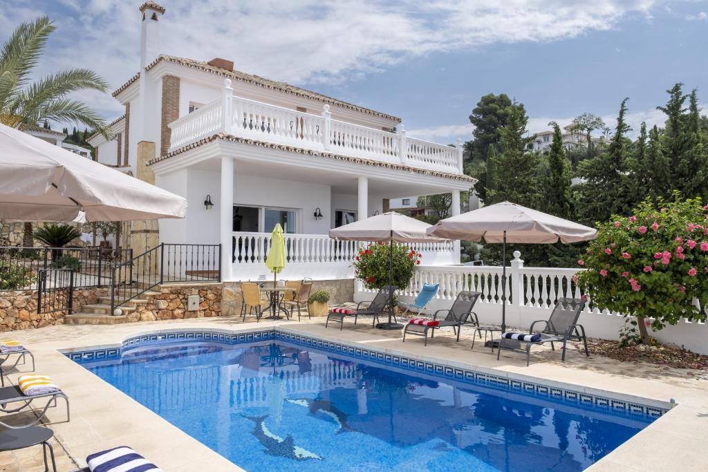 a pool with chairs and umbrellas in front of a house at Casa Montelado in Mijas