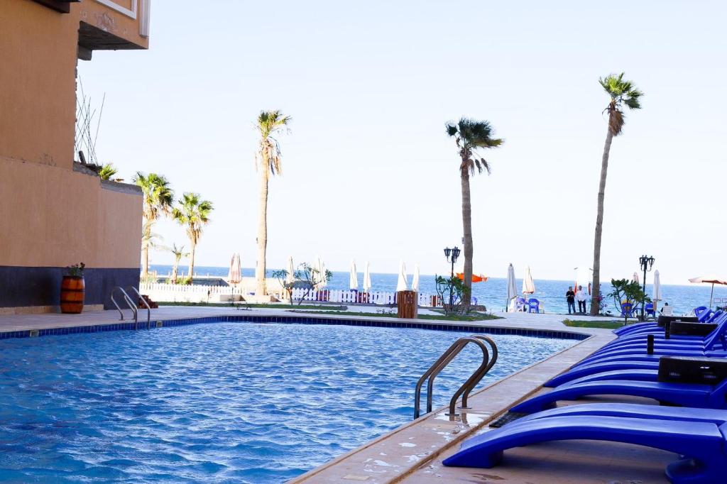 a swimming pool with blue chairs and palm trees at Juliana Beach Elite Queen T Collection in Hurghada