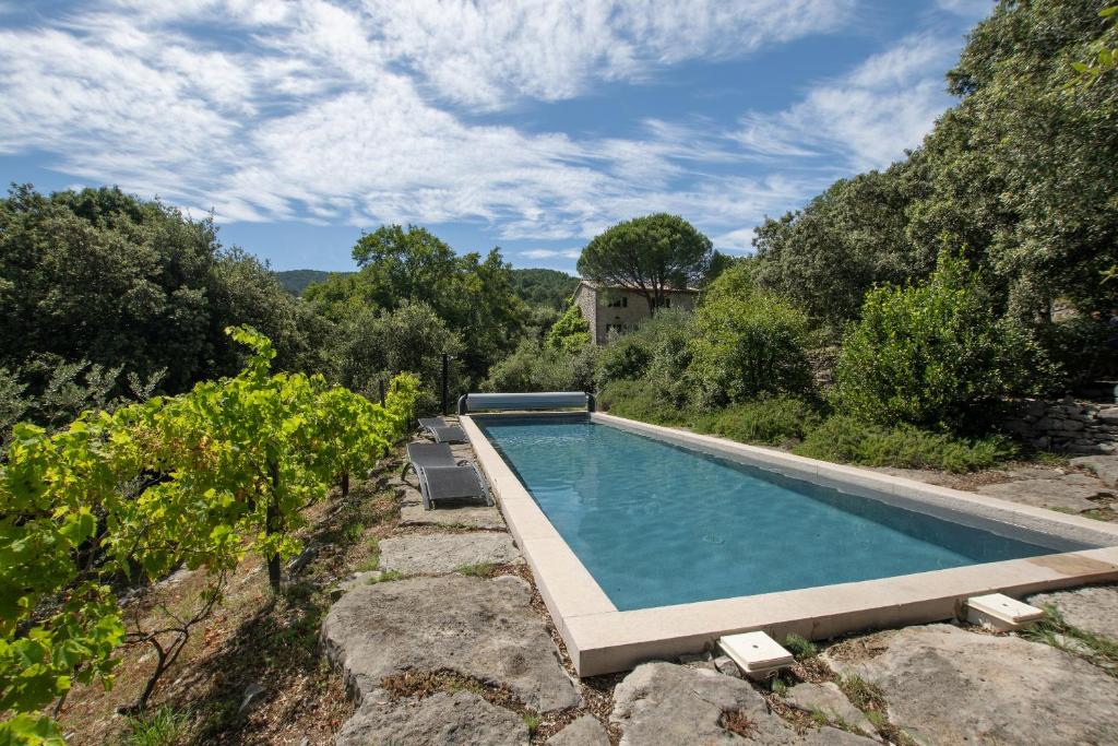 a swimming pool in a garden with trees and a house at Villa L'Elzède in Les Vans