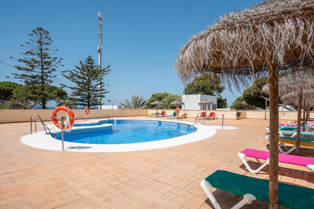 a swimming pool with chairs and a straw umbrella at Apartamento En Los Caños De Meca in Los Caños de Meca