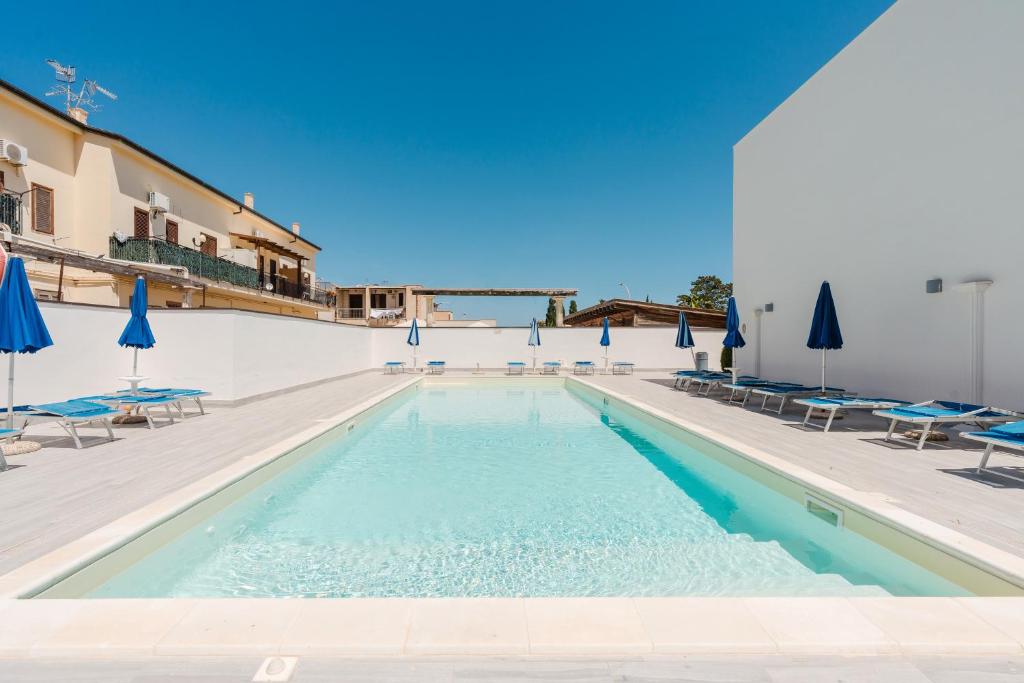 a swimming pool with chairs and blue umbrellas at Kairos San Vito Lo Capo in San Vito lo Capo