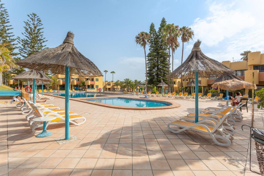 a resort with a pool with chairs and umbrellas at Casa Del Caballero Corralejo in Corralejo