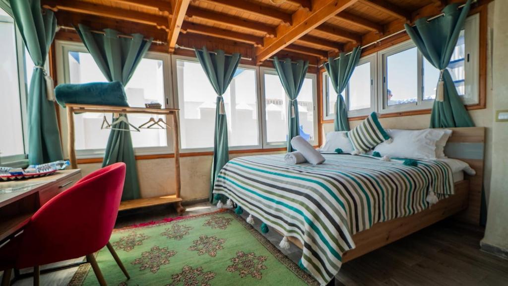 a bedroom with a bed and a desk and windows at Nid de médina Studio terrasse vue océan- Essaouira in Essaouira