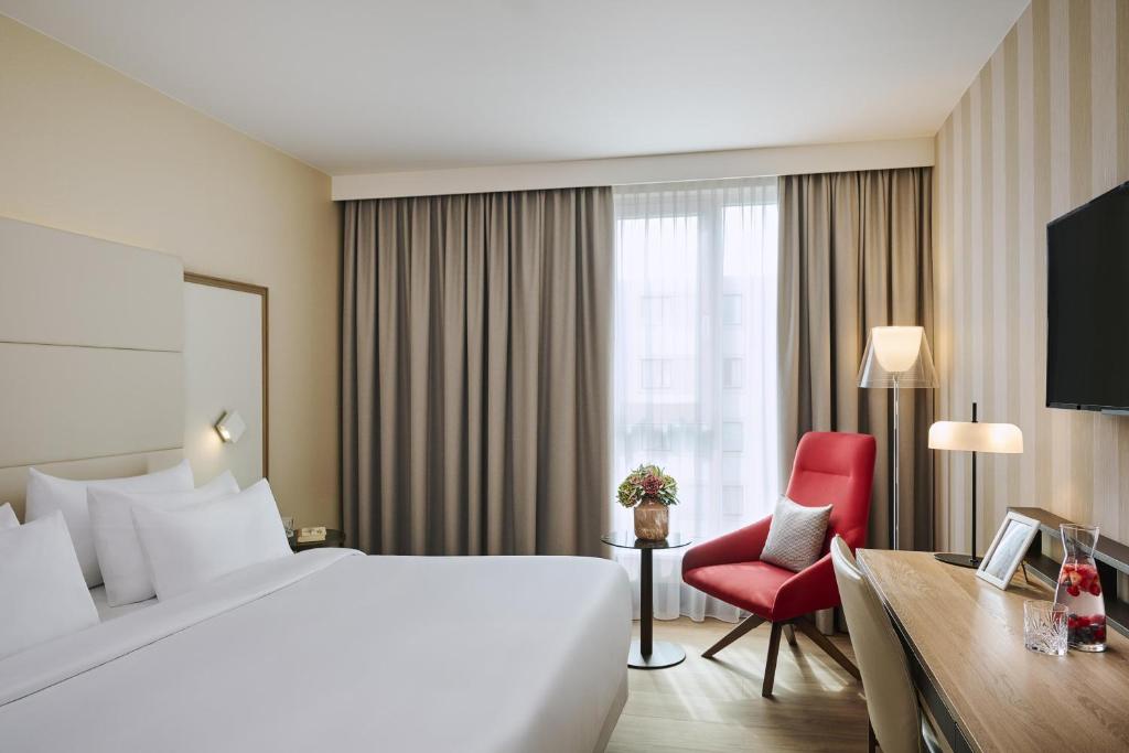 a hotel room with a bed and a red chair at NH Collection Nürnberg City in Nuremberg