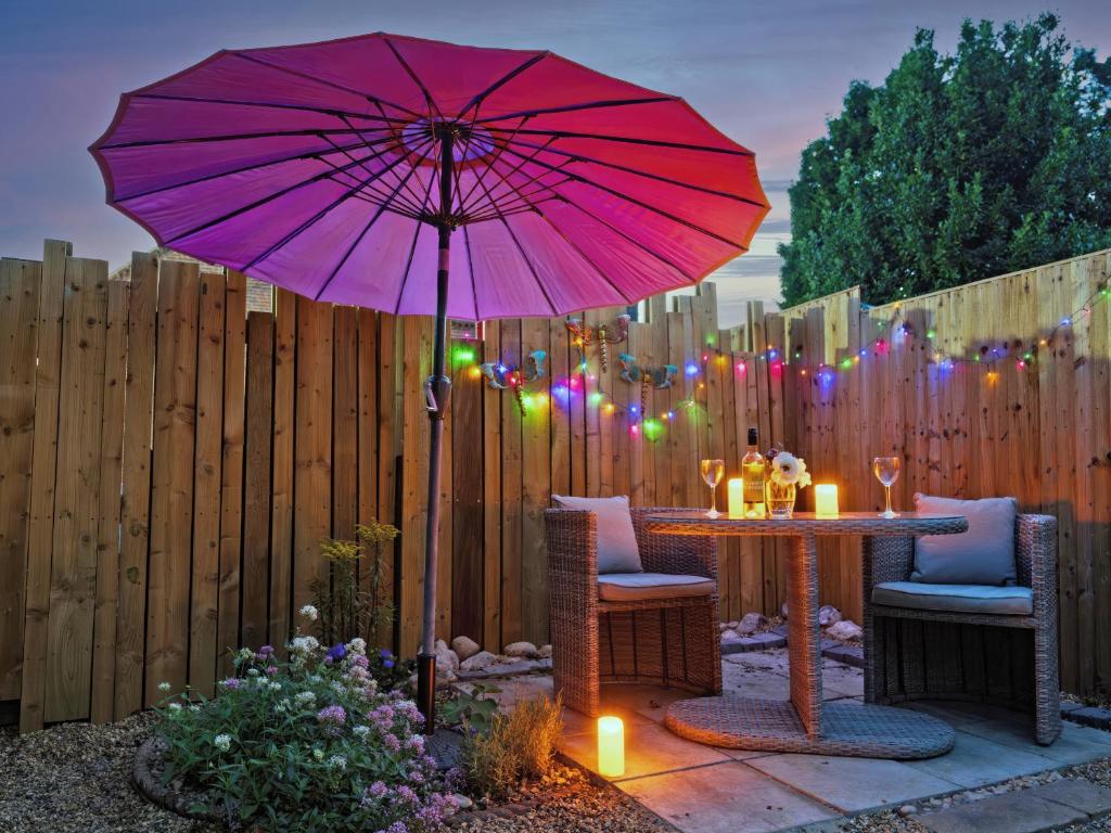 a patio with a table with a pink umbrella at Painter's Cottage in Hemsby