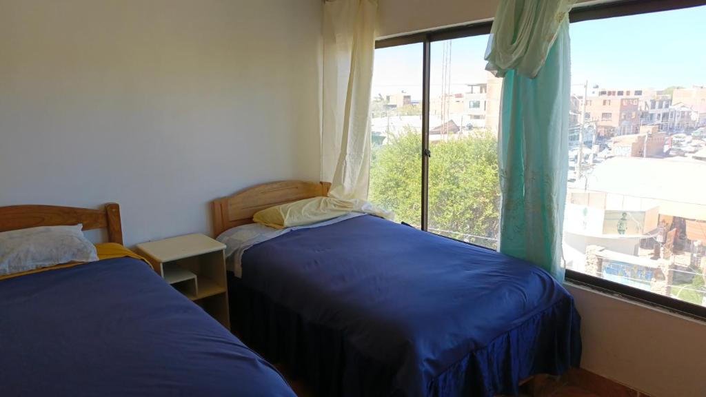 two beds in a room with a large window at Hostal la POSADA in Uyuni