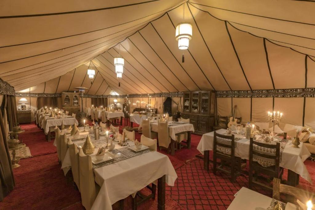 un comedor con mesas blancas y sillas en una tienda de campaña en Best Desert Luxury Camp, en Merzouga