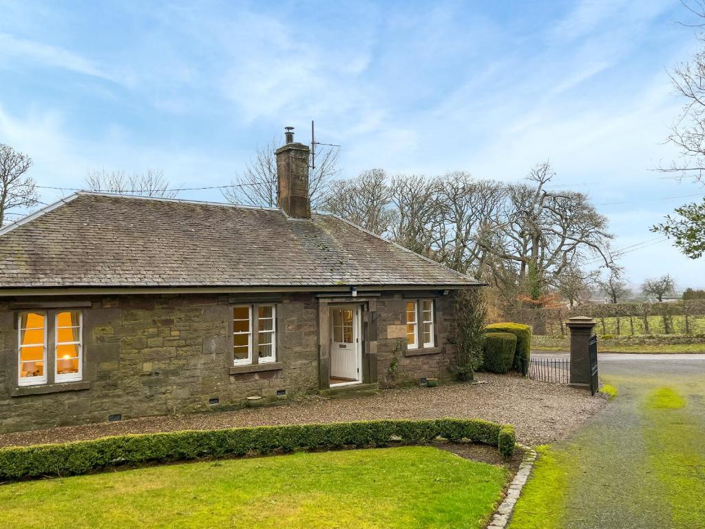 una pequeña casa de piedra con un patio de césped en Baldowrie Lodge, en Ardler