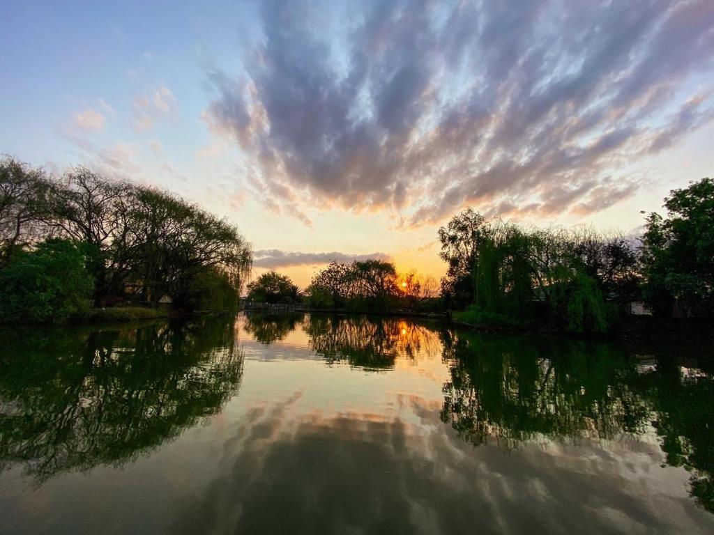 un coucher de soleil sur une rivière avec des arbres et des nuages dans l'établissement The Nugget Guest Lodge, à Kempton Park