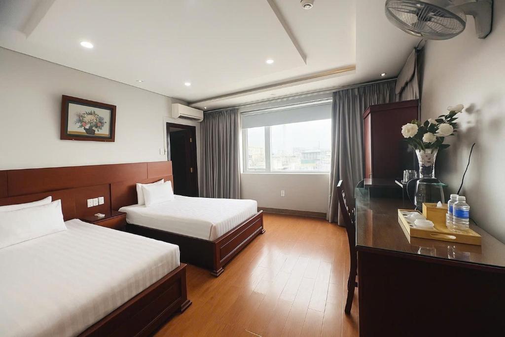 a hotel room with two beds and a desk with flowers at Van Ha Boutique Hotel Etown - Nhà Ga T3 in Ho Chi Minh City