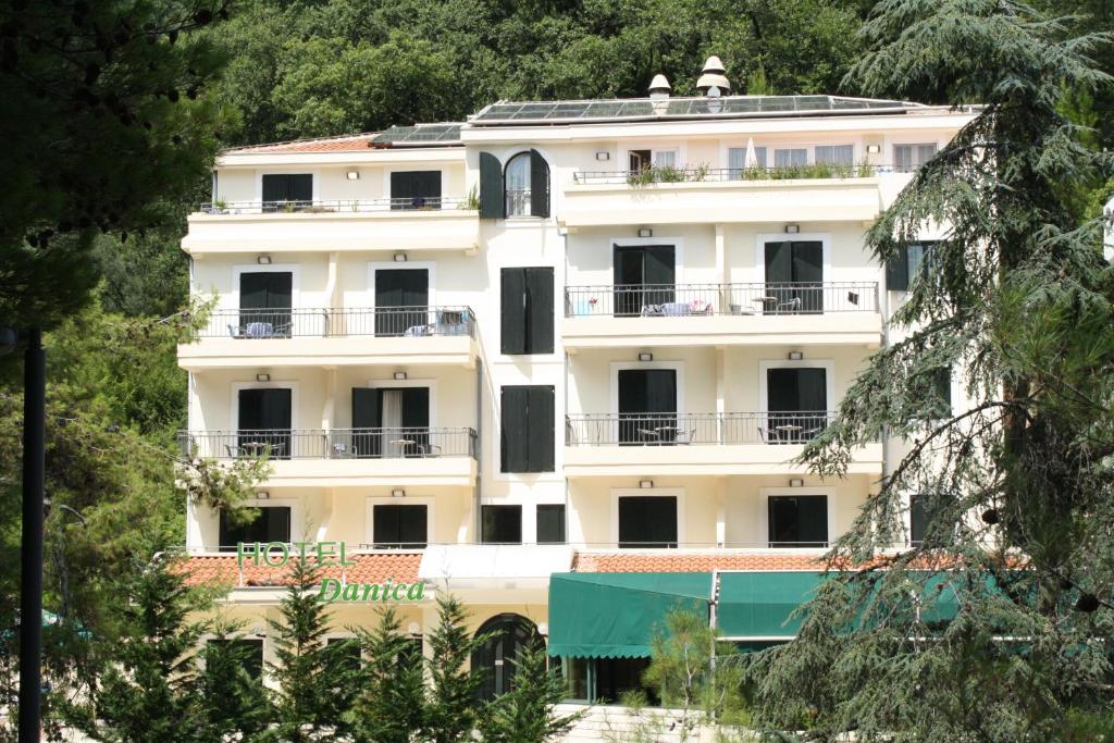 a white building with balconies and trees at Hotel Danica in Petrovac na Moru