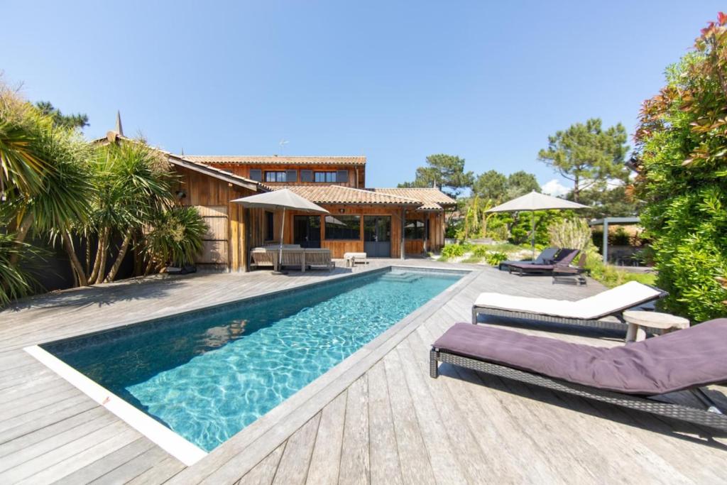 a swimming pool with two lounge chairs and a house at Villa Palombes au Cap Ferret charming villa with swimming pool in Cap-Ferret