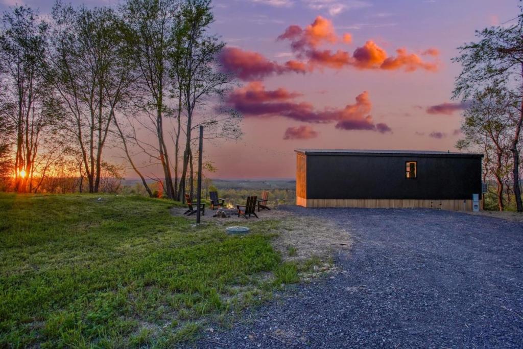 a small black building on a field with a sunset at Skyline Serenity - Hot Tub in Brookville