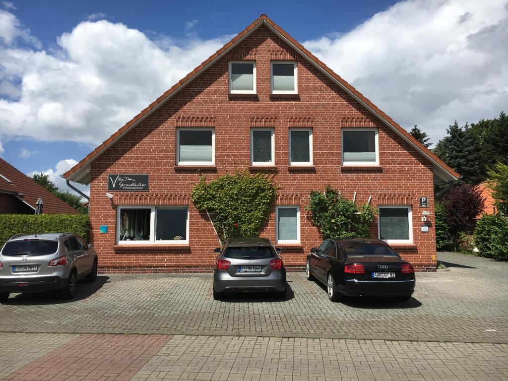 due auto parcheggiate di fronte a un edificio di mattoni di Pension Villa Strandläufer a Norddeich