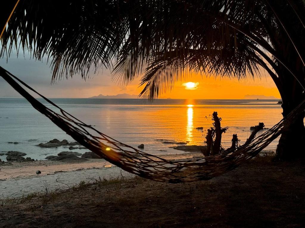 una hamaca en la playa con una puesta de sol en el fondo en Three Palms - Beach Front Tiny House by SP Villa, en Nathon Bay