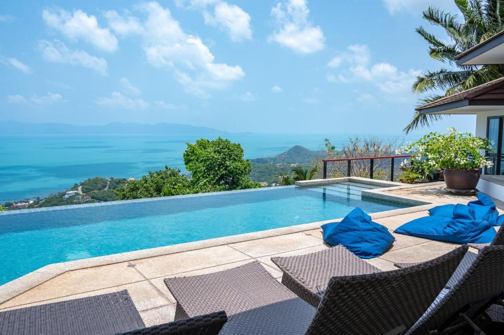 Villa Sawadee 5 by SP Villa Management في Nathon Bay: حمام سباحة مع الكراسي والمحيط في الخلفية