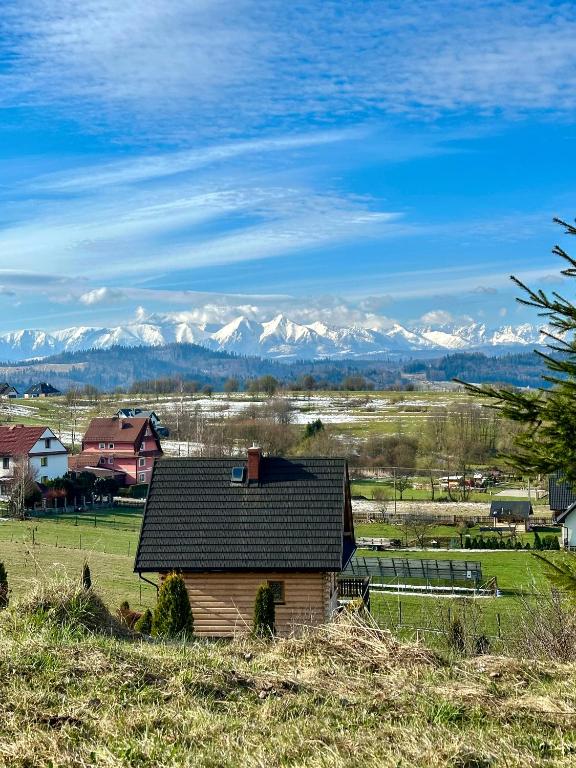 a small house in a field with mountains in the background at Pocztówka z Mizernej, drewniane domki, widok na Tatry, blisko Velo Czorsztyn, Jezioro Czorsztyńskie, rowery, spokojna okolica in Kluszkowce