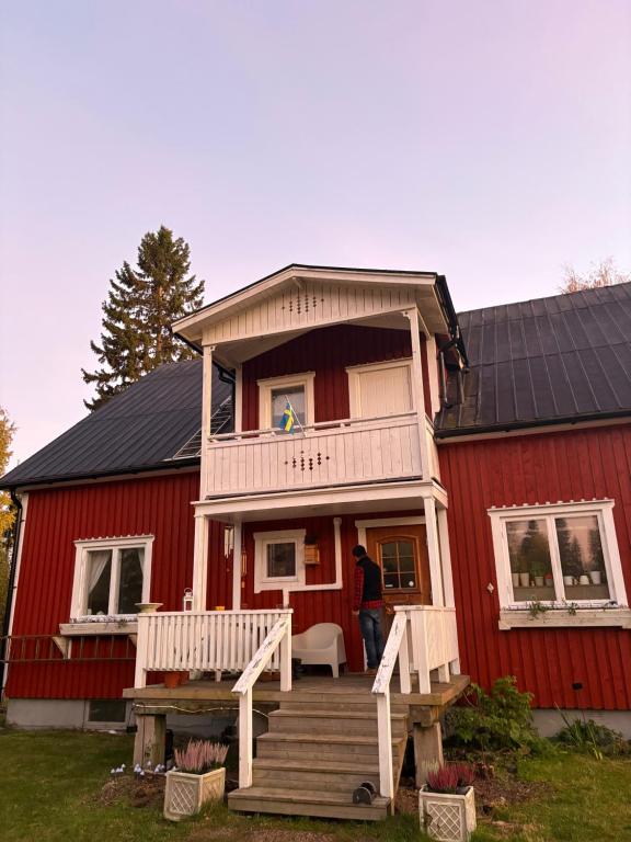 a man standing on the porch of a red house at Boreal Cottage in Karungi