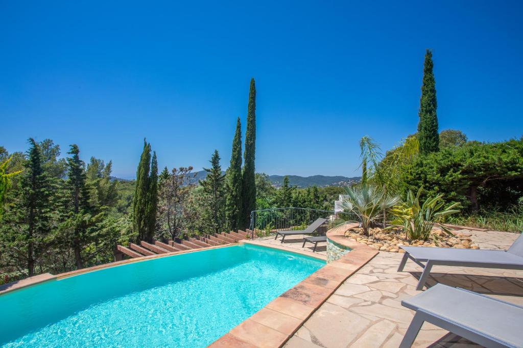 a swimming pool in a yard with two chairs and trees at Villa - La Colline in Saint-Raphaël