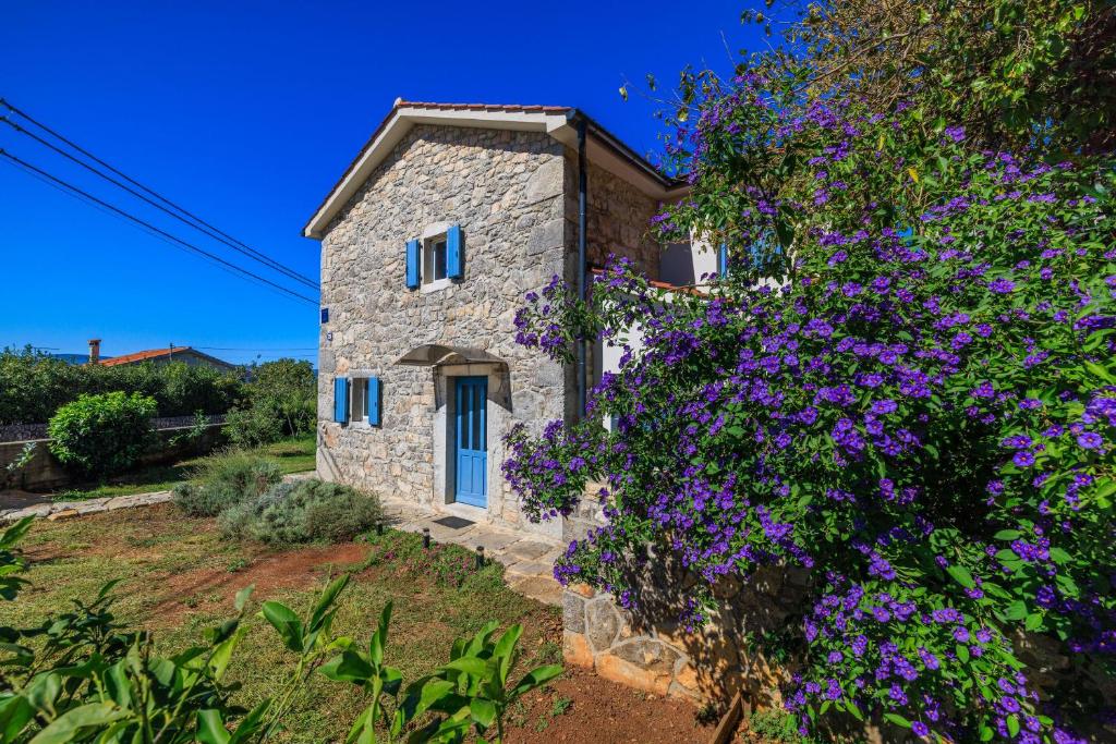 a stone house with blue windows and purple flowers at House Maja in Skrbčići
