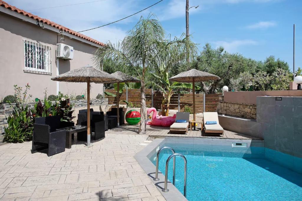 a swimming pool with umbrellas and chairs next to a house at Villa Dionysia Studio S2 in Alikanas