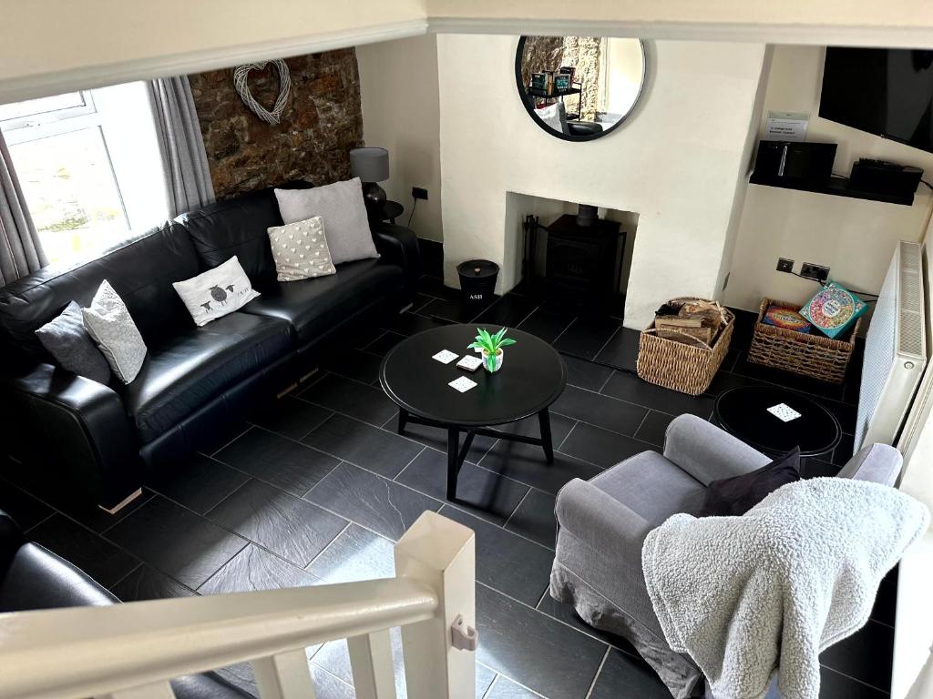 a living room with a black leather couch and a table at Port Eynon Beach Cottage in Port-Eynon